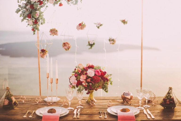 A table beautifully set with two sets of plates, spoons, towels, glasses, candles, flower bouquets, and more